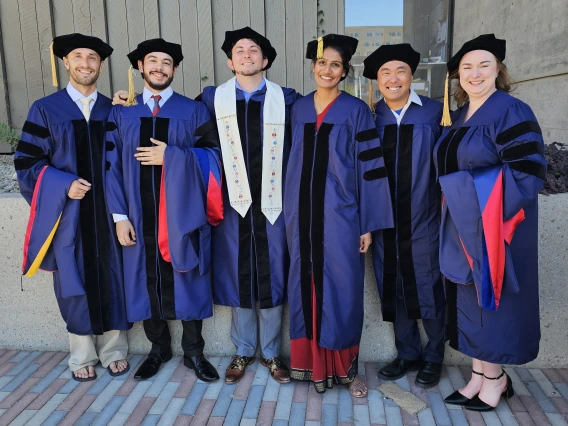 Six PhD students in caps and gowns celebrate graduation
