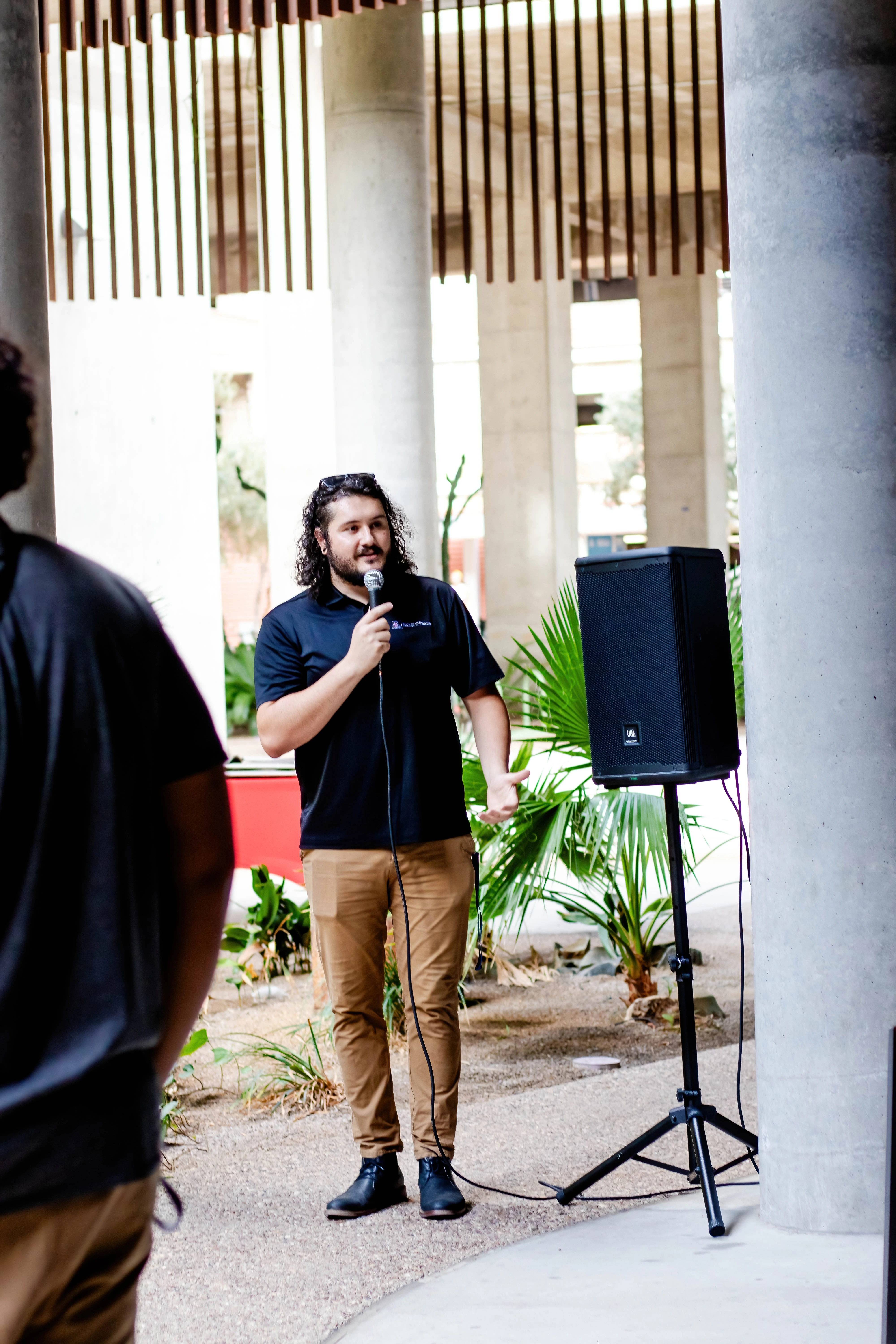 Collin Stout speaking into a microphone at the Welcome Event likely saying something profound