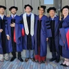 Six PhD students in caps and gowns celebrate graduation